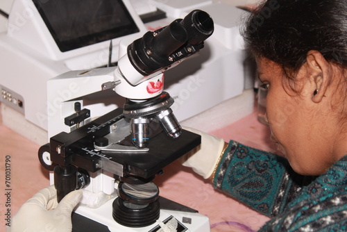 Lady pathologist examining with microscope. India