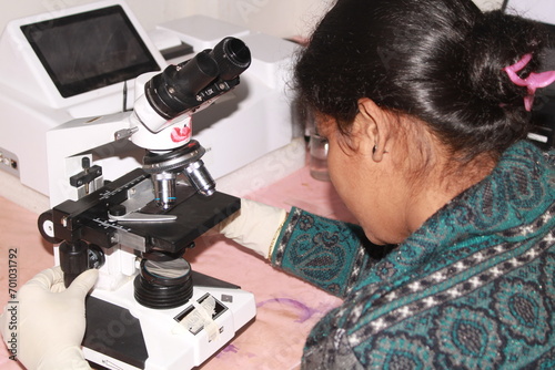 Lady pathologist examining with microscope. India