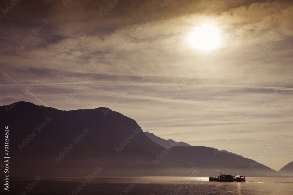 Boat sailing on lake during a dramatic sunrise. Lugano, Ticino, Switzerland
