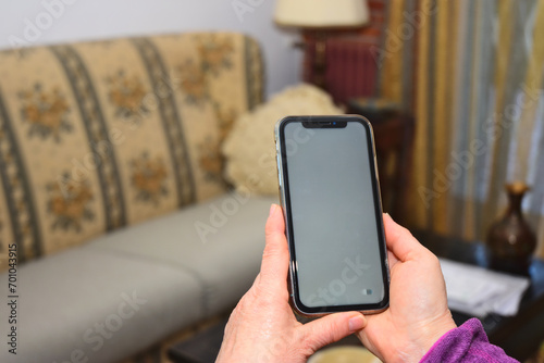 mani di una donna che tengono lo smartphone cellulare in casa in posizione decentrata, schermo bianco vuoto per testo, progettazione e pubblicità di app mobili online photo