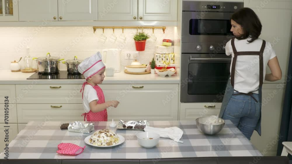mother and 3-year-old child in chef uniform preparing cake in home kitchen mother and 3-year-old child in chef uniform preparing cake in home kitchen