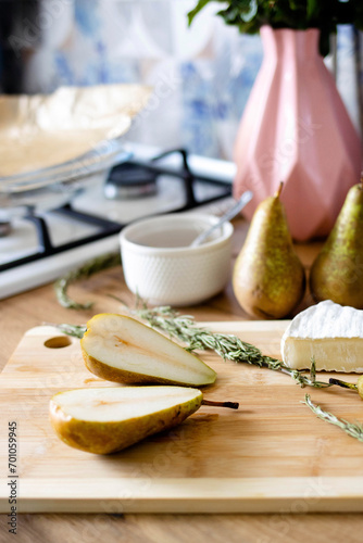 Sliced pear, cheese, and rosemary lie down on a wooden board against the background of a modern kitchen. Cooking concept