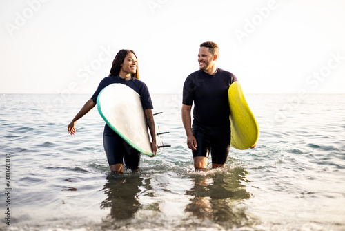 Two dark-skinned young men are coming out of the sea dressed in wetsuits while carrying surfboards. African couples surfers. Water sports. Boys look at each other at sunset.
