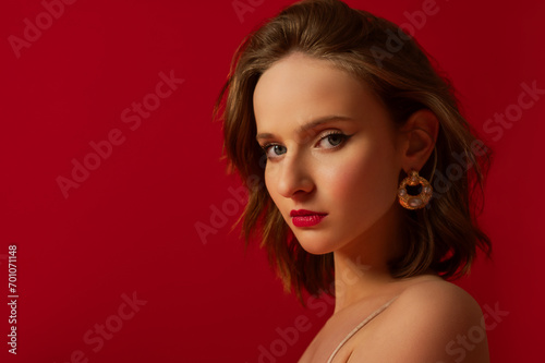 Young beautiful woman with red lips makeup wearing trendy pearl earrings, posing on red background. Close up studio portrait. Copy, empty space for text