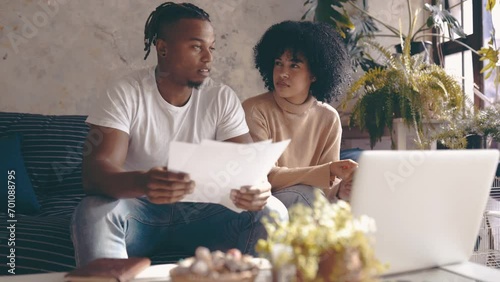 Black couple, laptop and documents in financial debt, budget planning or expenses on sofa at home. African man and woman with paperwork on computer for finance, bills or invoice together at house photo