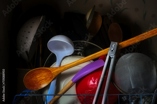 A typical Kitchen scene in almost every American household. Spoon, ladle, tongs, scraper, bowls, and other kitchenware pile up on the side of the sink to dry.
