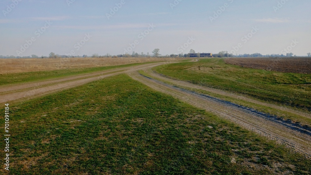A clear sky overlooks an open field with a curving, tire-marked path.