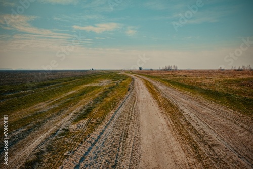 A dirt road curves through a grassy field, leading into the distance under a clear sky.