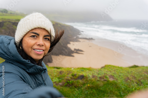 Latina woman with knit hat enjoying a beautiful views of the wild Irish coast on a windy day © Alberto Marrupe