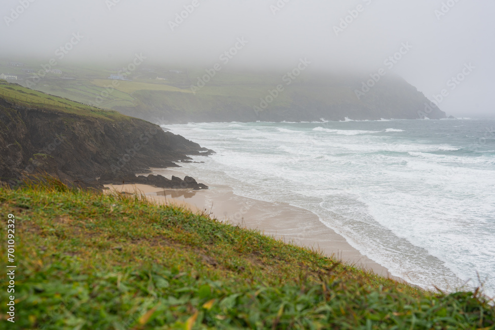 Landscape seen from a beach cliff with strong waves and fog in the background on the Irish coast