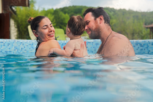 Father and mother teaching small child swimming in the pool.