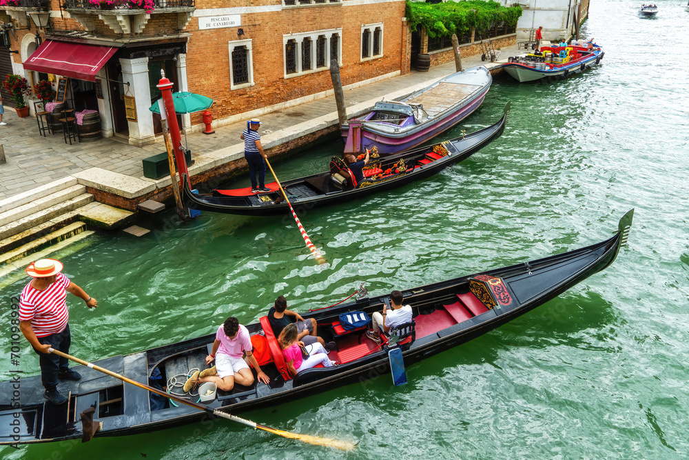 Venetian gondolier punting gondola through green canal waters of Venice. - obrazy, fototapety, plakaty 