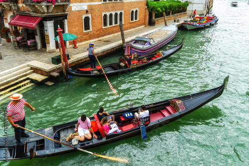 Venetian gondolier punting gondola through green canal waters of Venice. photo