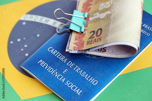 Brazilian work card and social security blue book and reais money bills on flag of Federative Republic of Brazil close up photo
