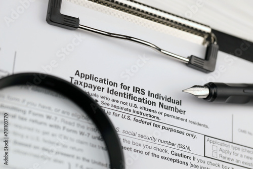 IRS Form W-7 Application for IRS Individual taxpayer identification number, blank on A4 tablet lies on office table with pen and magnifying glass close up photo