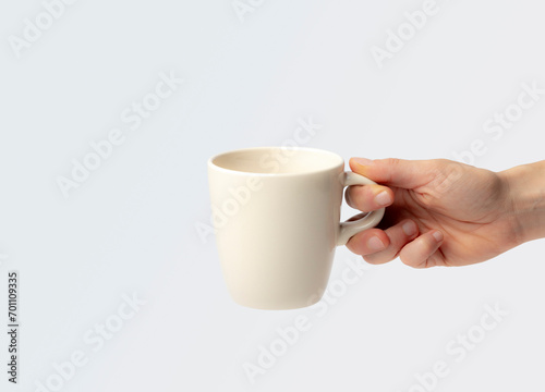 Mockup of a cup, held by a young woman's hand, as if waiting to be filled with hot coffee, or chocolate, on a plain background