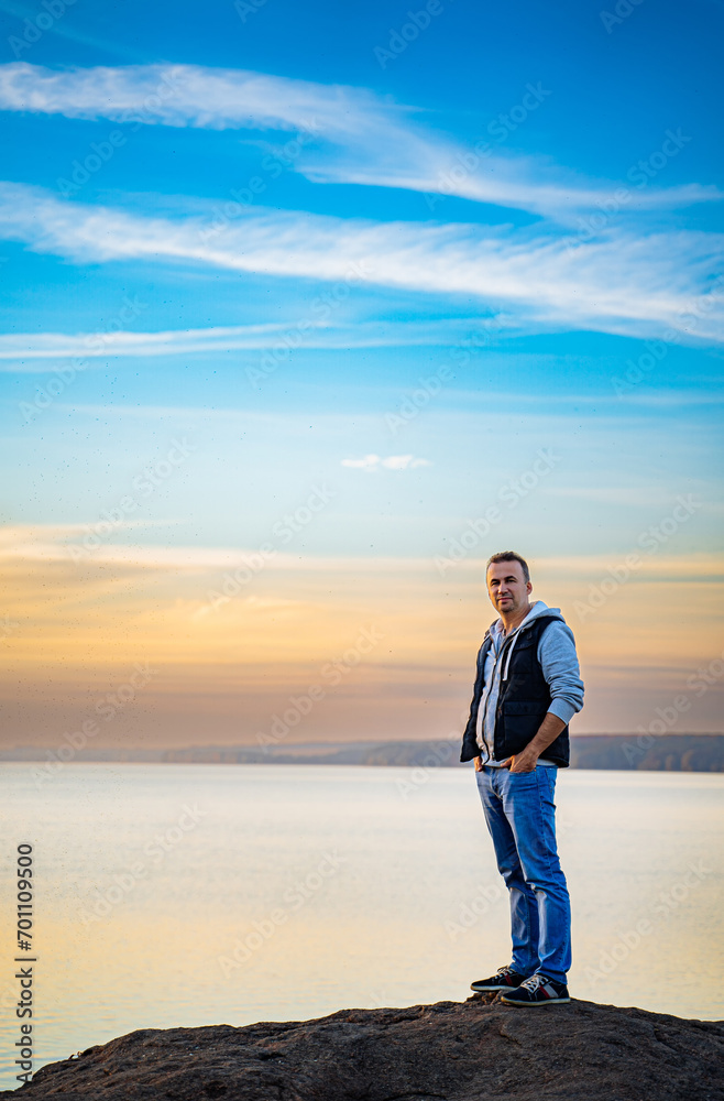 Man Enjoying Serene View of Water from atop Rock. A man standing on top of a rock next to a body of water Man Enjoying Serene View of Water from atop Rock. A man standing on top of a rock next to a body of water