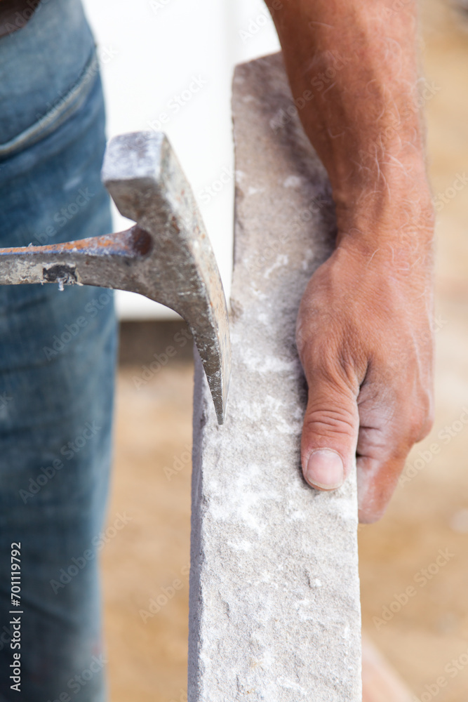 Close up of mason holding piece of stone and a hammer. Stone mason.