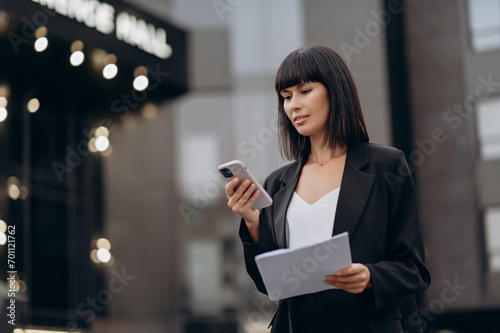 Business woman using smartphone. A young woman walks through the city with a cup of coffee and a telephone.