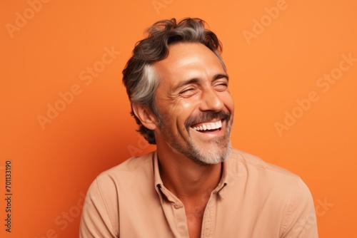 Portrait of happy mature man laughing and looking at camera on orange background © Igor