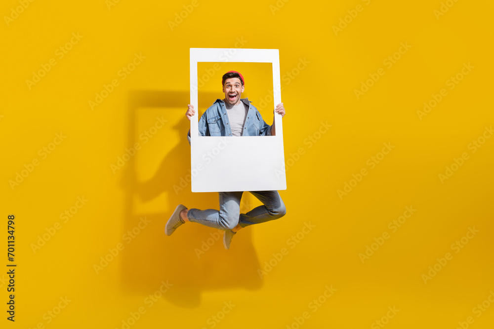 Full length photo of funky cheerful man dressed jeans shirt jumping high taking photo isolated yellow color background - obrazy, fototapety, plakaty 