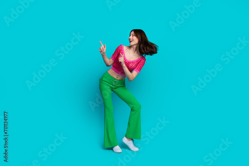 Full length photo of cheerful woman dressed knitwear top green pants directing look at promo empty space isolated on blue color background