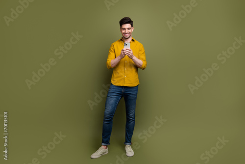 Full length photo of cheerful handsome man wear stylish clothes writing comment facebook instagram isolated on khaki color background