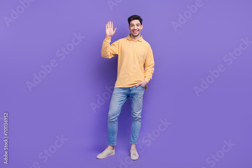 Full size photo of attractive young man waving hand greeting friendly wear trendy yellow clothes isolated on violet color background © deagreez
