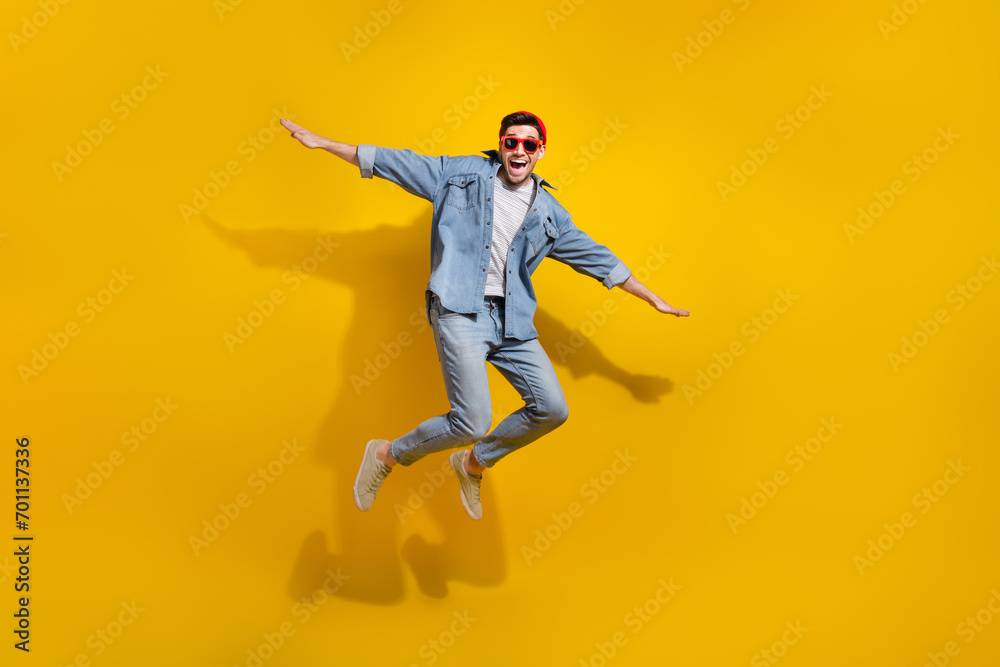 Full length photo of good mood carefree man dressed jeans shirt dark spectacles jumping high isolated yellow color background