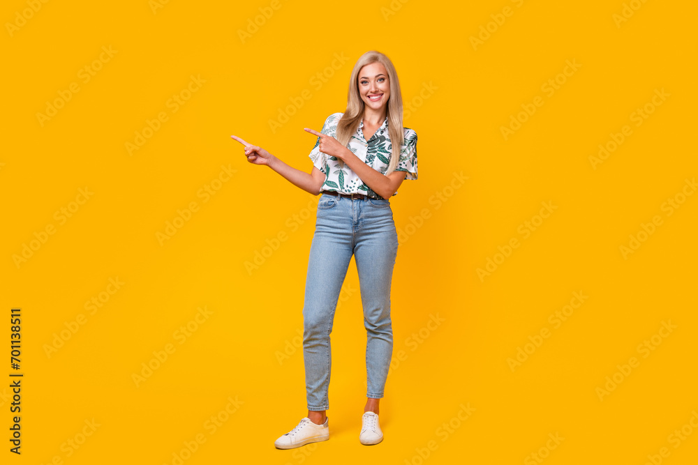 Full length photo of adorable woman wear stylish blouse denim pants indicating at discount empty space isolated on yellow color background Full length photo of adorable woman wear stylish blouse denim pants indicating at discount empty space isolated on yellow color background