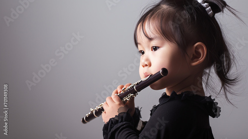 Cute toddler Asian girl kid in black dress playing flute isolated on gray background with copy space  studio shot of child portrait with space for text.