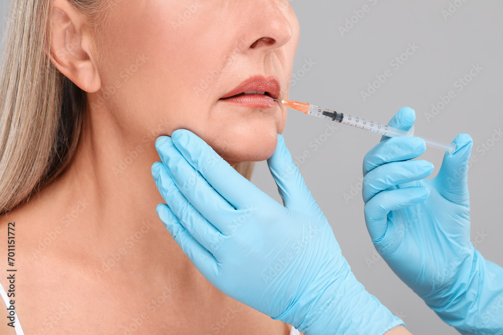 Doctor giving lips injection to senior woman on light grey background, closeup. Cosmetic surgery Doctor giving lips injection to senior woman on light grey background, closeup. Cosmetic surgery