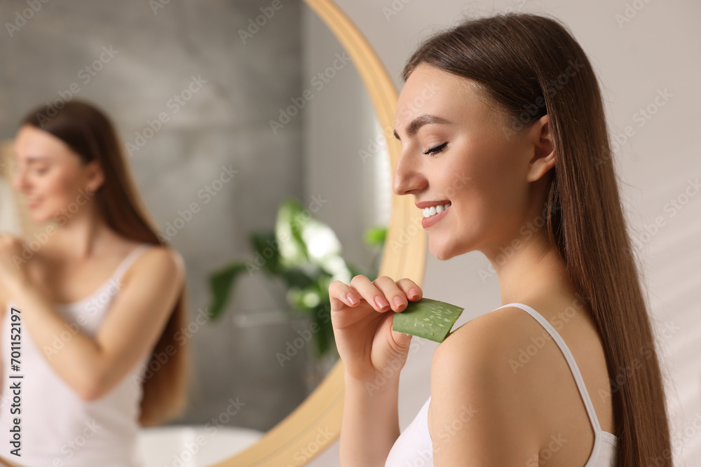 Young woman applying aloe gel from leaf onto her shoulder in bathroom. Space for text