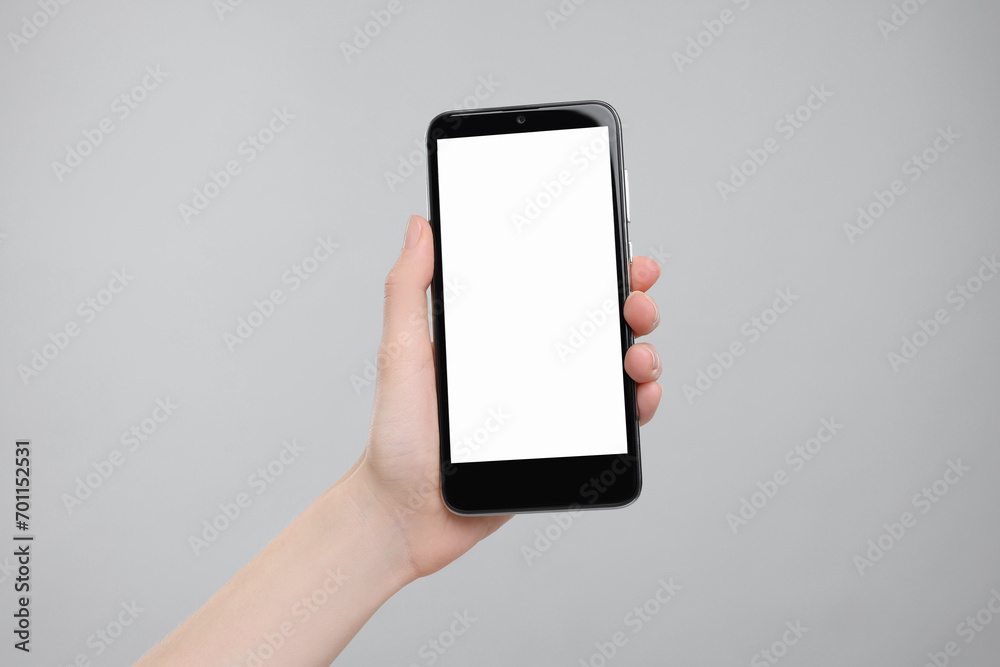 Woman holding smartphone with blank screen on grey background, closeup. Mockup for design Woman holding smartphone with blank screen on grey background, closeup. Mockup for design