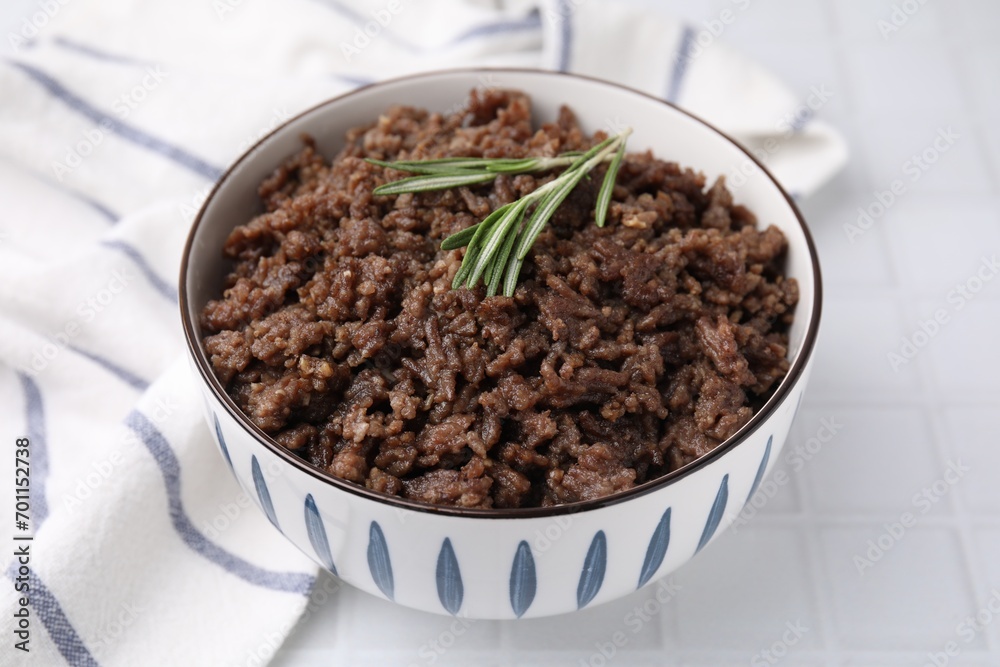 Fried ground meat in bowl and rosemary on white tiled table, closeup Fried ground meat in bowl and rosemary on white tiled table, closeup