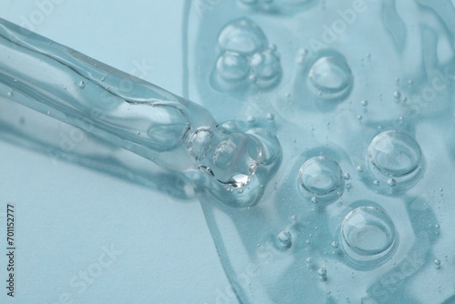 Dripping cosmetic serum from pipette onto light blue background, macro view