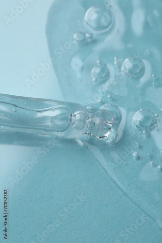Dripping cosmetic serum from pipette onto light blue background, macro view © New Africa