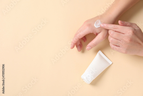 Woman with tube applying cosmetic cream onto her hand on beige background, top view. Space for text