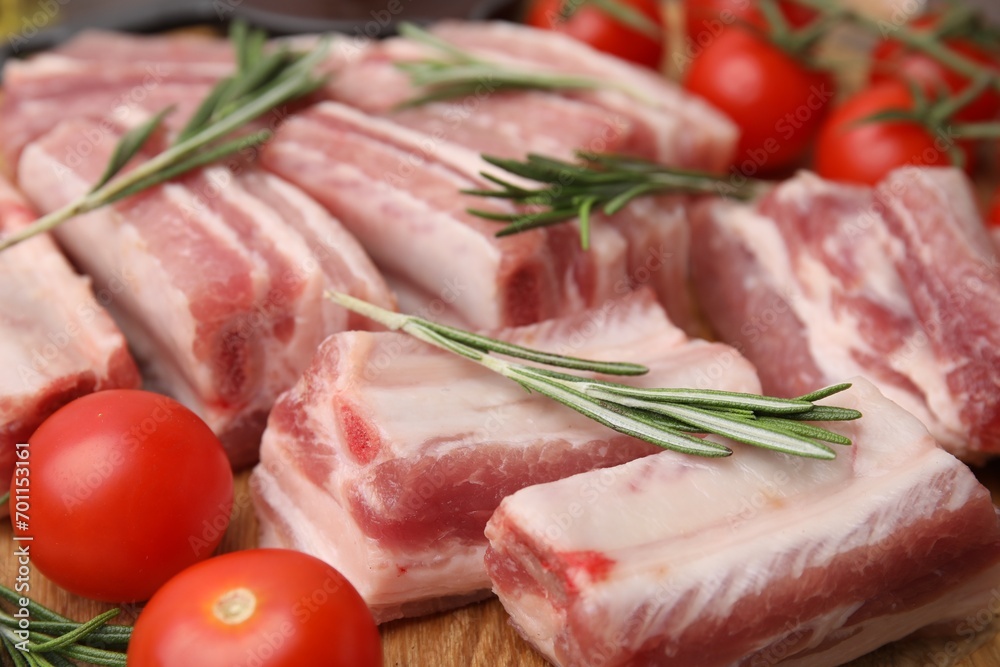 Cut raw pork ribs with rosemary and tomatoes on wooden board, closeup Cut raw pork ribs with rosemary and tomatoes on wooden board, closeup