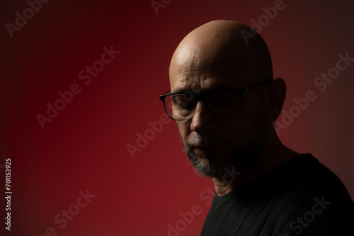 Handsome, bald, bearded man in prescription glasses looking down.