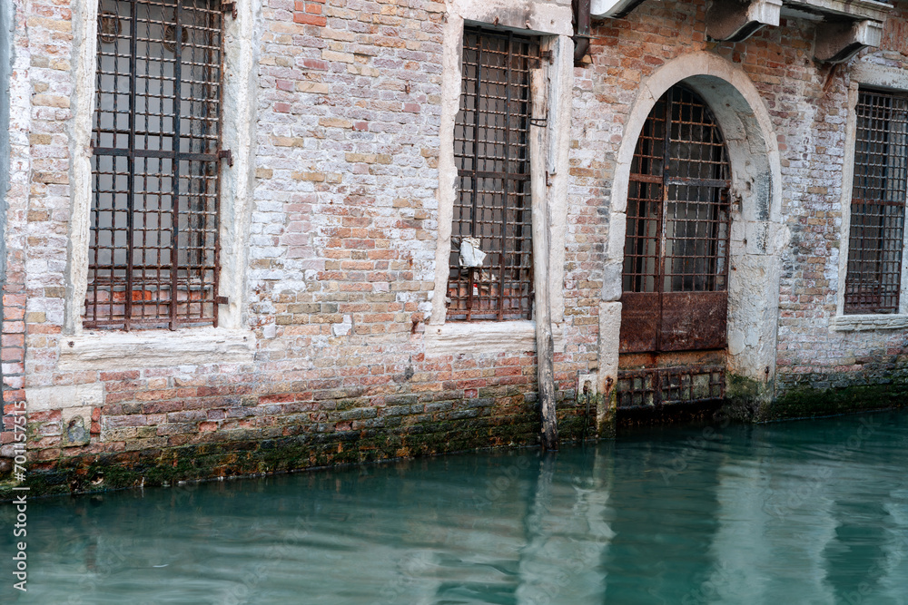 Old brick building with security protected window and door alongside and reflected in green water of canal. Old brick building with security protected window and door alongside and reflected in green water of canal.