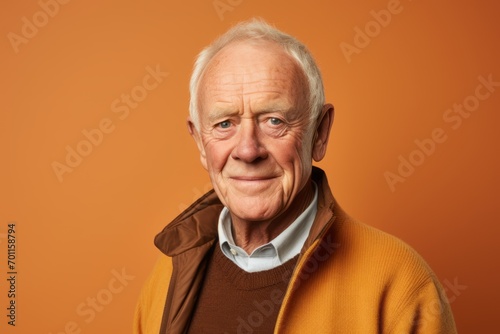 Portrait of an elderly man in a yellow sweater on an orange background