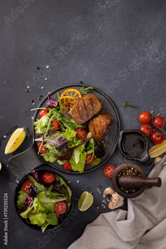 pieces of Organic grilled Tuna Steak on black ceramic serving dish with salad on a table