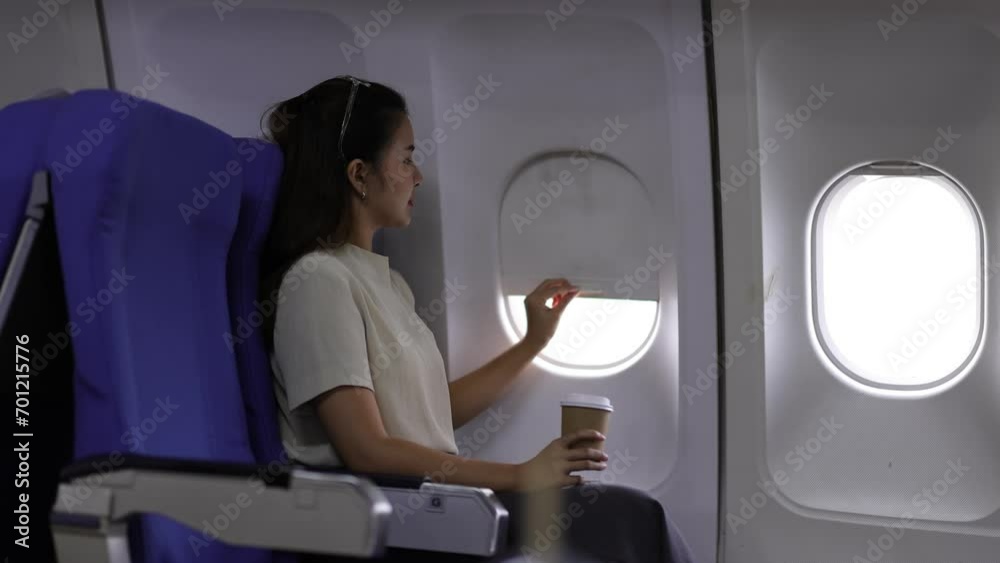 A young Asian woman sitting in the window seat of a commercial airliner and leans back with her eyes closed resting. A young Asian woman sitting in the window seat of a commercial airliner and leans back with her eyes closed resting.