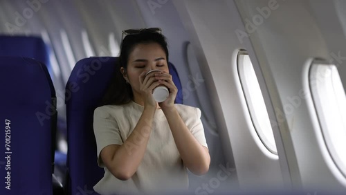 Young Asian female tourist traveling alone on a plane is drinking hot coffee and looking out the window. photo