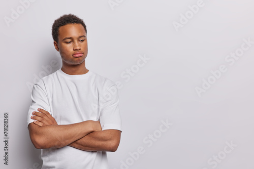 Sulking upset dark skinned man keeps arms folded being dissatisfied with something has sad thoughtful expression wears casual t shirt isolated over white background copy space for your promotion