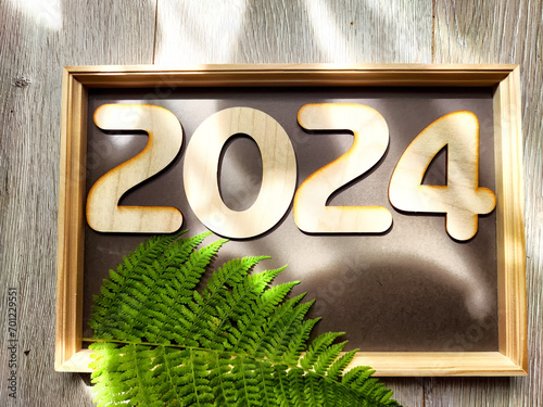 Wooden figures and numbers of the new year 2024 with frame and green fern leaves. Celebration. Abstract background, pattern, frame, place for text and copy space photo