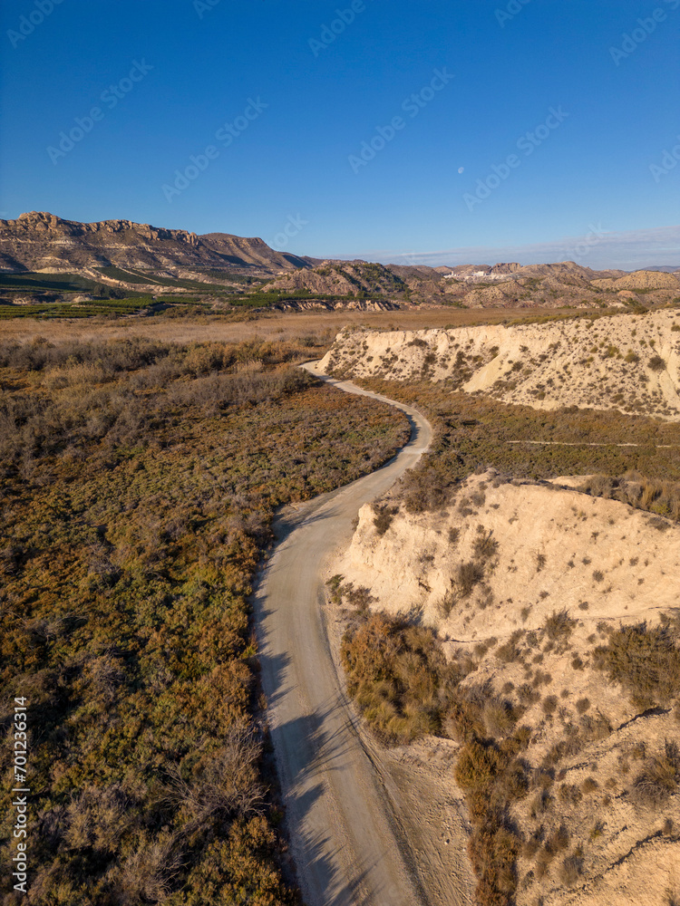 Dirt road in arid desert landscape with distant cliffs and morning sunlight, Elche, Alicante province, Spain - Stock photo