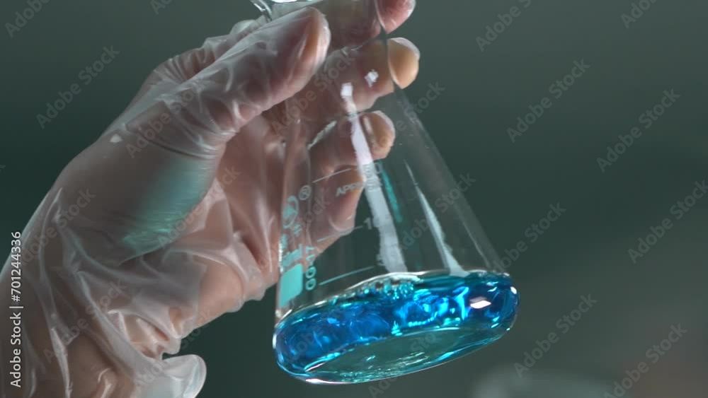 A scientist's hand shakes a flask with a blue liquid in a medicinal chemistry laboratory