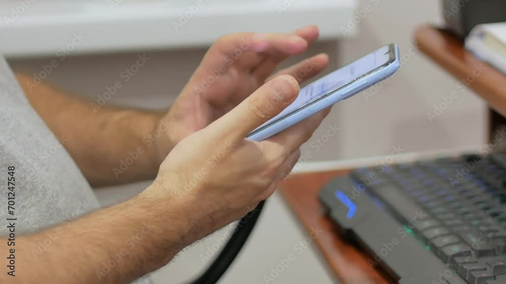 A man sitting at a desktop computer at home or in the office is holding a blue phone in his hands. Work at home or in the office, remotely. A man sitting at a desktop computer at home or in the office is holding a blue phone in his hands. Work at home or in the office, remotely.
